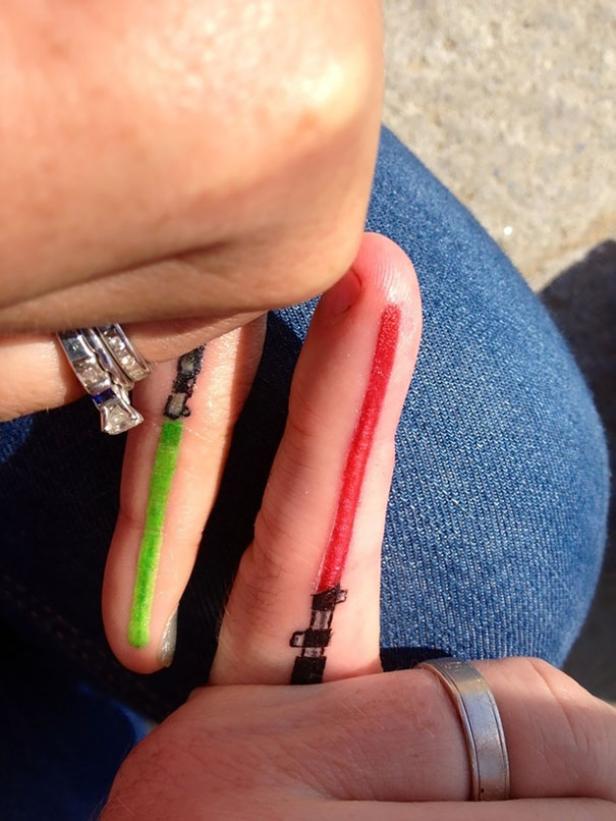 Zwei Finger mit Tätowierungen, die grüne und rote Lichtschwerter darstellen.