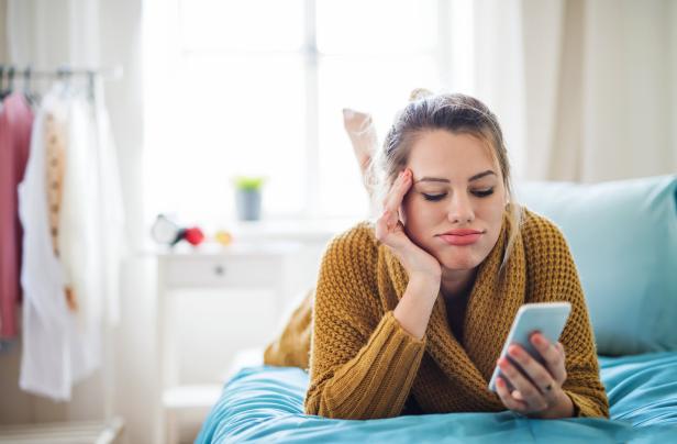 Eine Frau liegt frustriert mit einem Handy auf dem Bett.