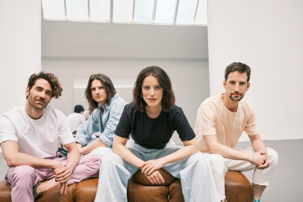Die Band Silbermond sitzt auf einer braunen Couch vor einer weißen Wand.