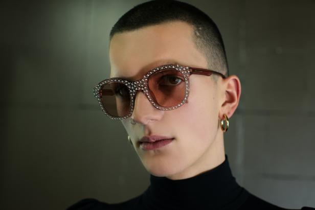 Eine Person mit Ohrringen und Nasenring trägt eine mit Strasssteinen besetzte Sonnenbrille.