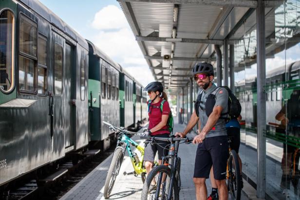 Zwei Radfahrer warten mit ihren Fahrrädern auf einem Bahnsteig auf den Zug.