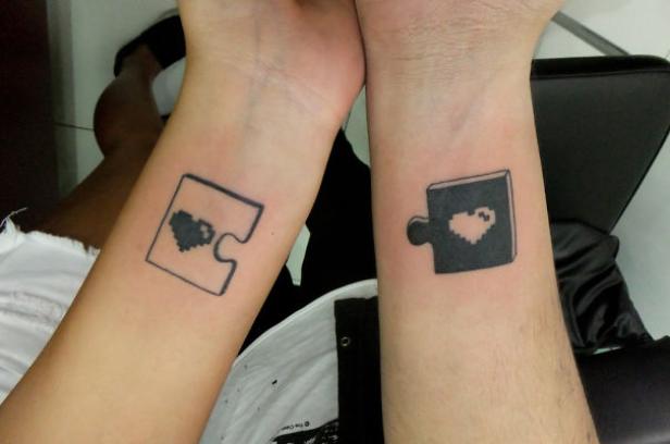 Zwei Handgelenke mit passenden Puzzle-Tattoos, die jeweils ein Herz enthalten.