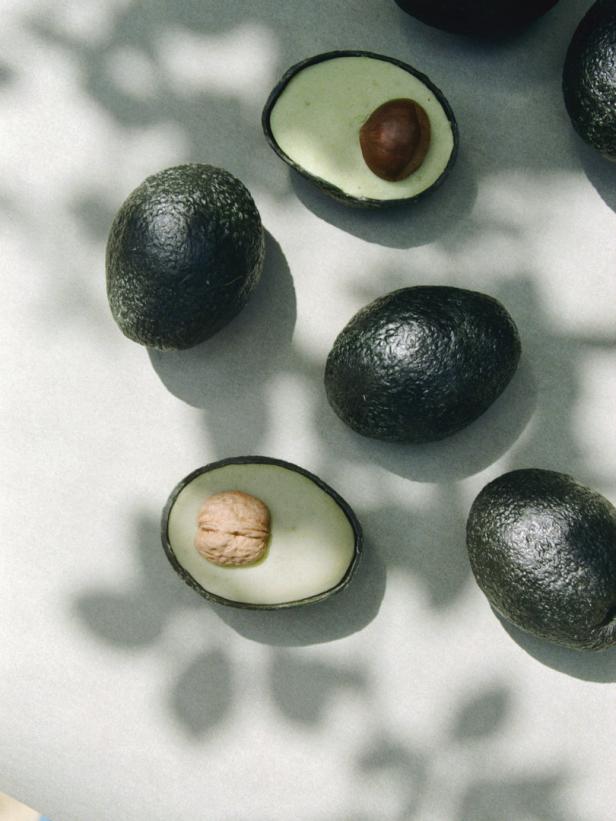 Mehrere Avocados, einige davon halbiert, liegen auf einer hellen Oberfläche.