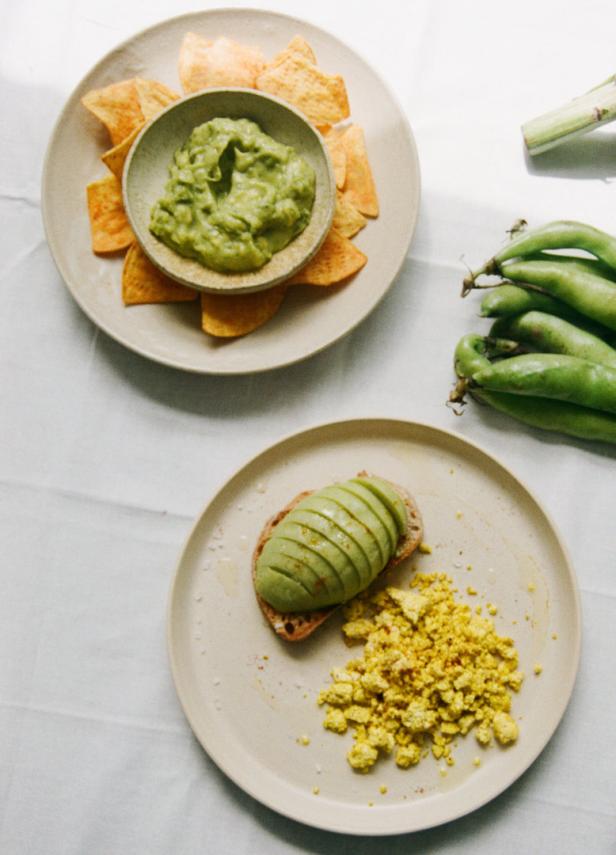 Zwei Teller mit Guacamole, Tortilla-Chips, Avocado-Toast und Rührei-Tofu.