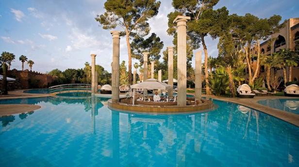 Ein Pool mit einer Barinsel, umgeben von Säulen und tropischer Vegetation.