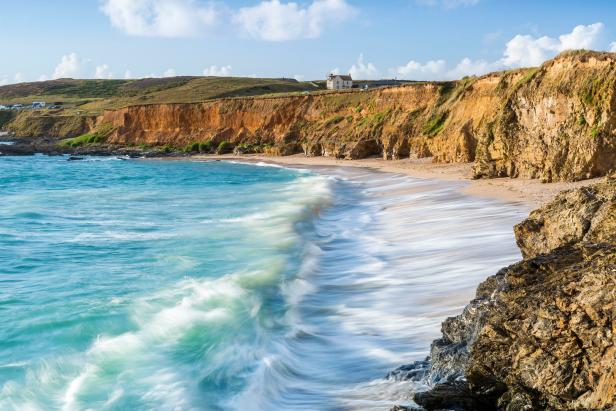 Türkisfarbenes Wasser umspült einen Sandstrand mit Klippen im Hintergrund.