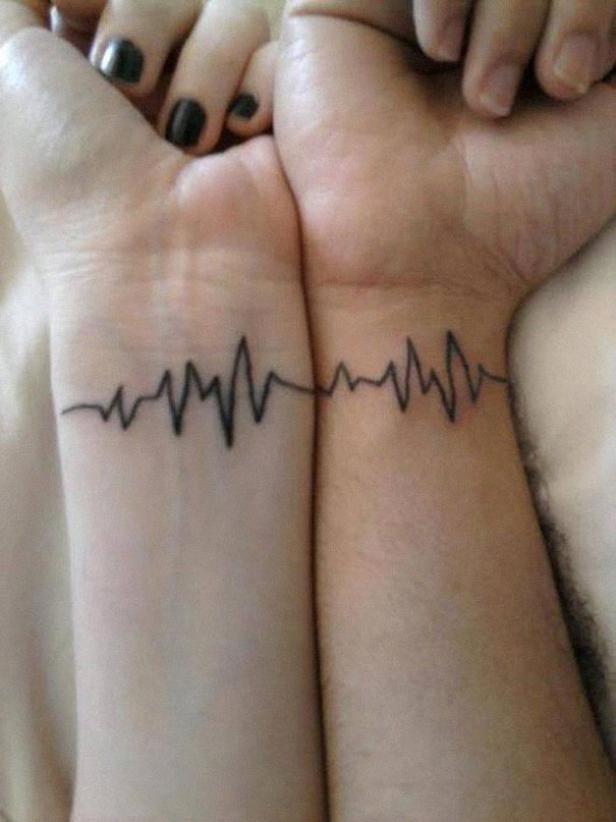 Zwei Handgelenke mit passenden EKG-Tätowierungen, die eine durchgehende Linie bilden.