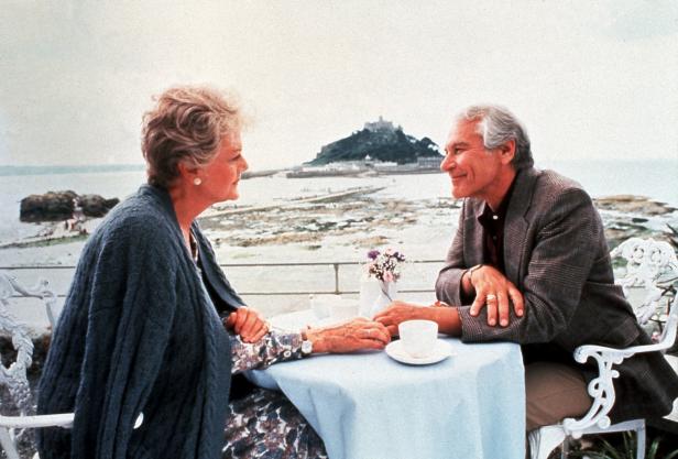 Ein älteres Paar sitzt an einem Tisch mit Blick auf das Meer und eine Insel mit einer Burg.