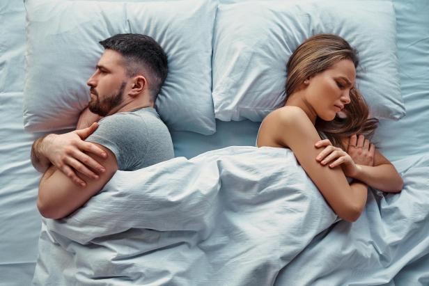 Junges, schönes Paar, das im Bett lag, drehte sich Rücken an Rücken, die Arme vor Wut und Groll verschränkt. Beziehungsprobleme. Draufsicht.