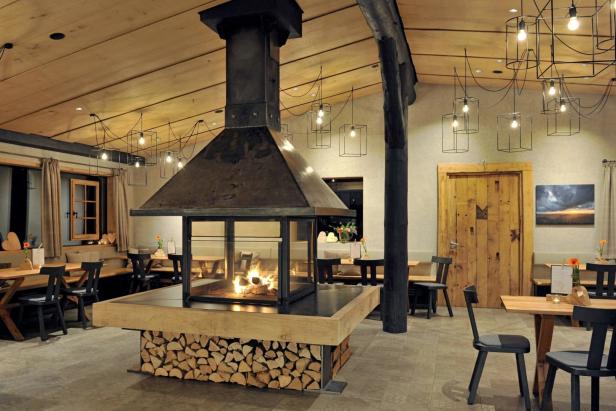 Ein Kamin mit Holzstapel in einem Restaurant mit Holztischen und Stühlen.
