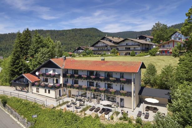Ein Hotel mit roten Ziegeln und blühenden Blumenkästen vor bewaldeten Hügeln.