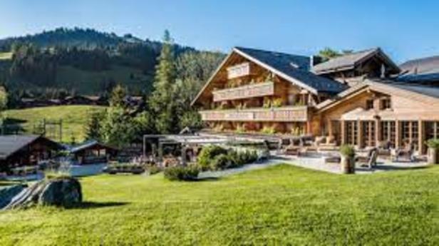Ein großes Holzhotel liegt in einer grünen Landschaft mit Bergen im Hintergrund.