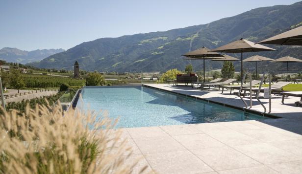 Ein Schwimmbad mit Liegestühlen und Sonnenschirmen vor einer Bergkulisse.