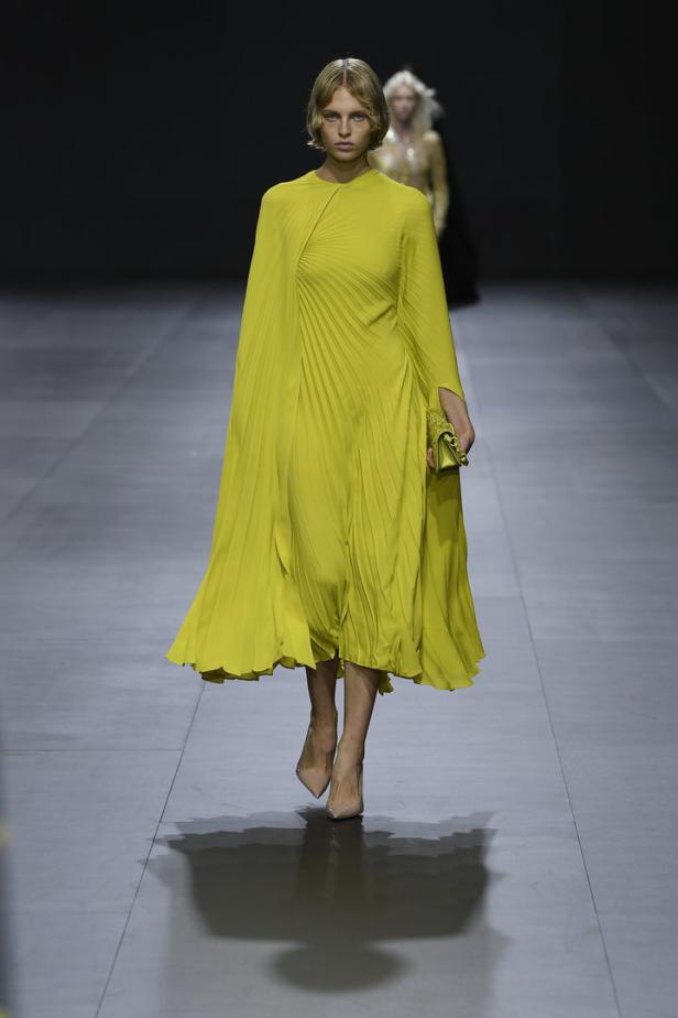 Eine Frau in einem plissierten, limonengelben Kleid auf einem Laufsteg.