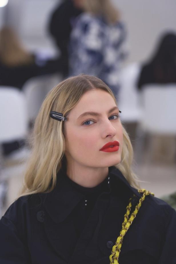 Eine blonde Frau mit roten Lippen und einer Haarspange im Haar blickt in die Kamera.