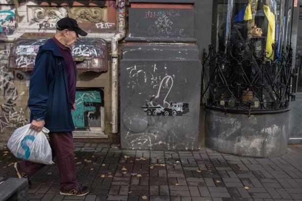 Ein Mann geht an einem Gebäude mit Graffiti und einem Banksy-ähnlichen Kunstwerk vorbei.