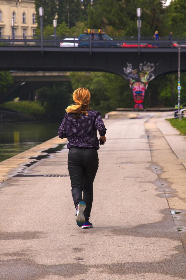 Eine Frau joggt auf einem Weg entlang eines Flusses in der Stadt.