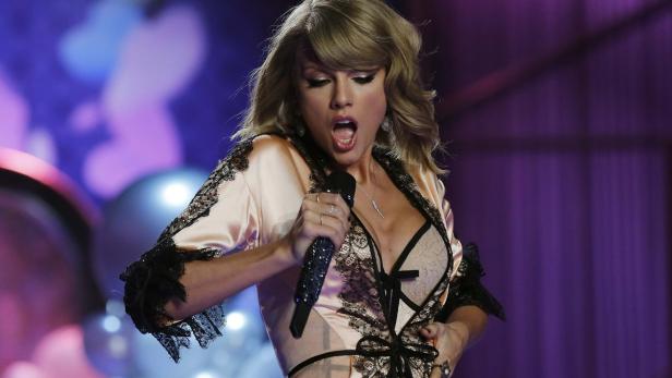 Taylor Swift singt in einem rosa Negligé mit schwarzer Spitze auf der Bühne.