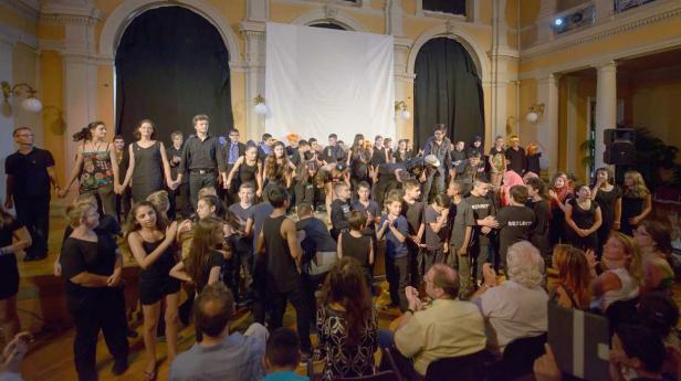 Eine Gruppe von Kindern und Erwachsenen verbeugt sich auf einer Bühne vor einem Publikum.