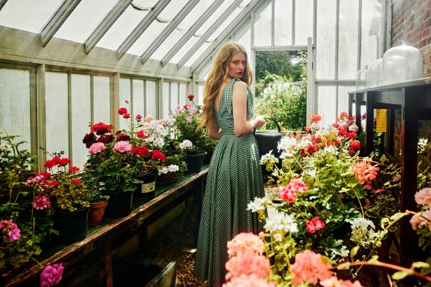 Eine Frau in einem grünen Kleid gießt in einem Gewächshaus Blumen.