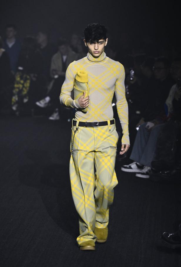 Ein Mann in einem karierten Rollkragenpullover und einer Hose auf einem Laufsteg.