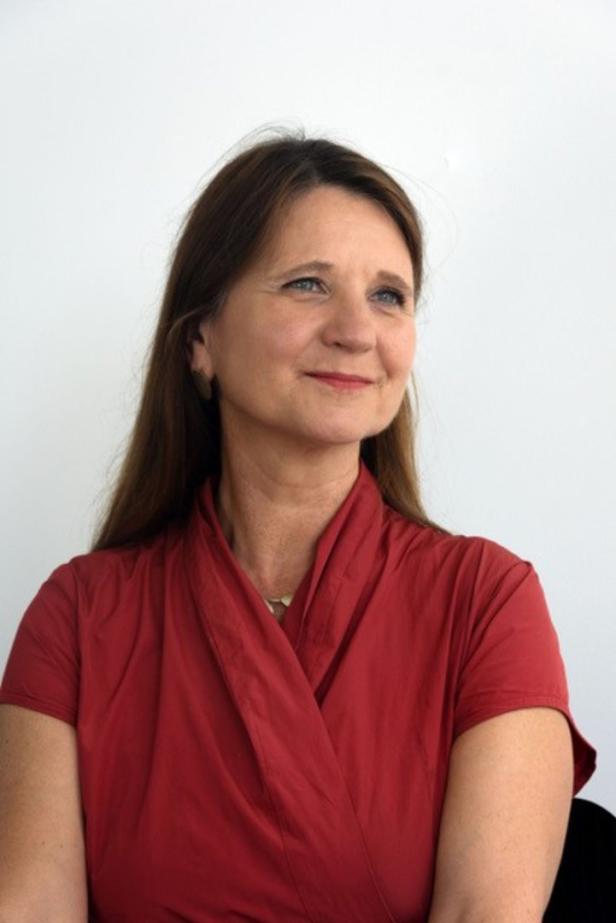 Eine Frau mit braunen Haaren und einem roten Oberteil blickt nach oben.