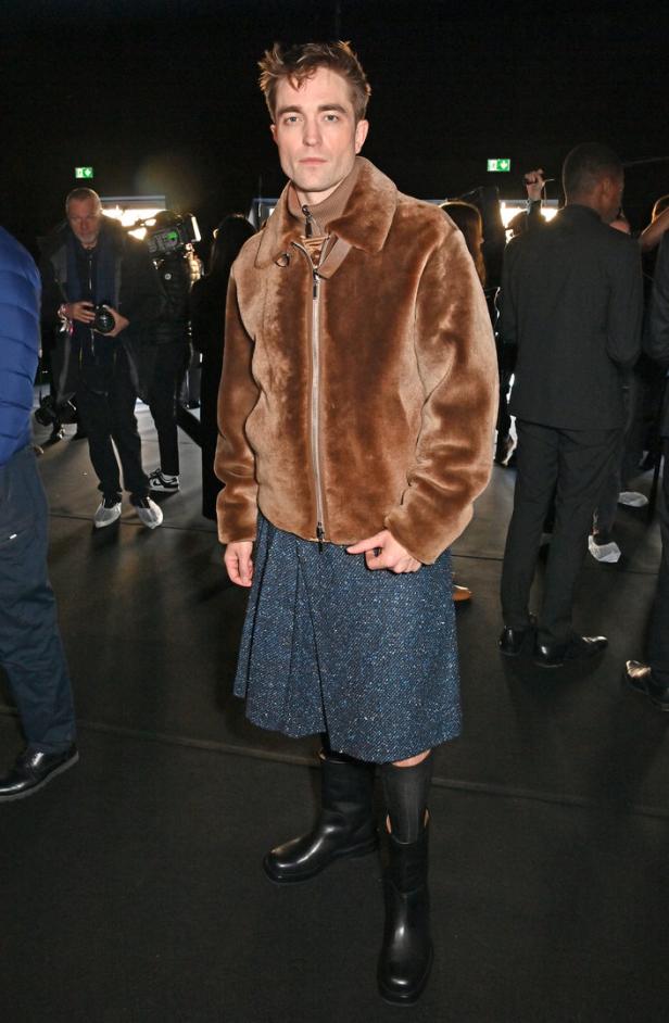 Robert Pattinson trägt eine Jacke aus Teddyfell, einen Rock und Gummistiefel.