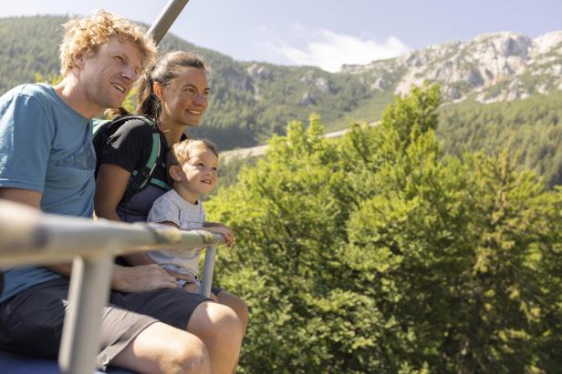 Eine Familie fährt in einer Seilbahn durch die Berge und genießt die Aussicht auf die umliegende Landschaft.