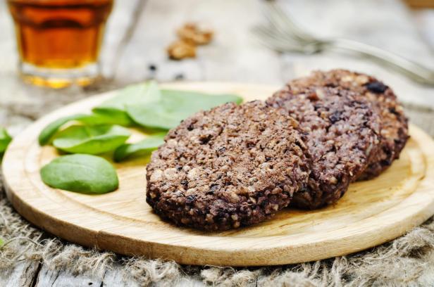 Drei Burger aus schwarzen Bohnen, Reis, Walnüssen und Hafer mit Spinat auf einem Holzbrett.