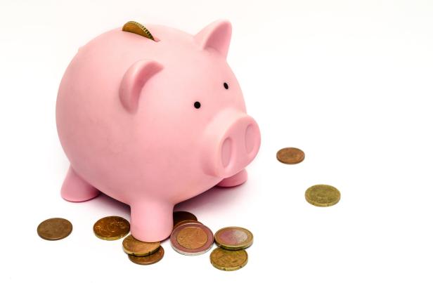 Ein rosa Sparschwein steht auf einem weißen Untergrund, umgeben von Euro-Münzen.