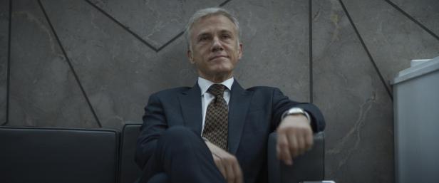 Christoph Waltz in der Serie The Consultant; er sitzt in einem Sessel und lächelt überlegen