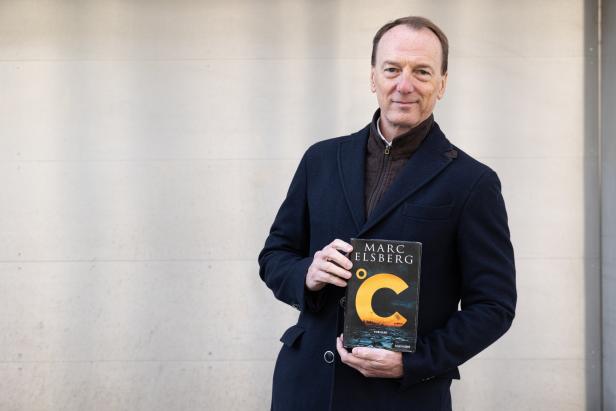 Ein Mann hält das Buch „°C – Thriller“ von Marc Elsberg in den Händen.