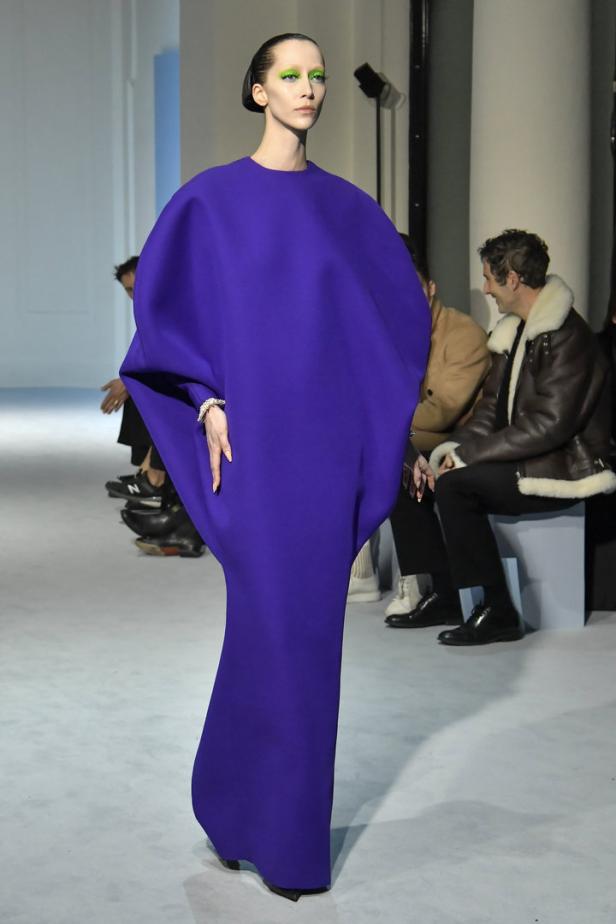 Eine Frau in einem violetten Kleid mit übergroßen Ärmeln auf einem Laufsteg.
