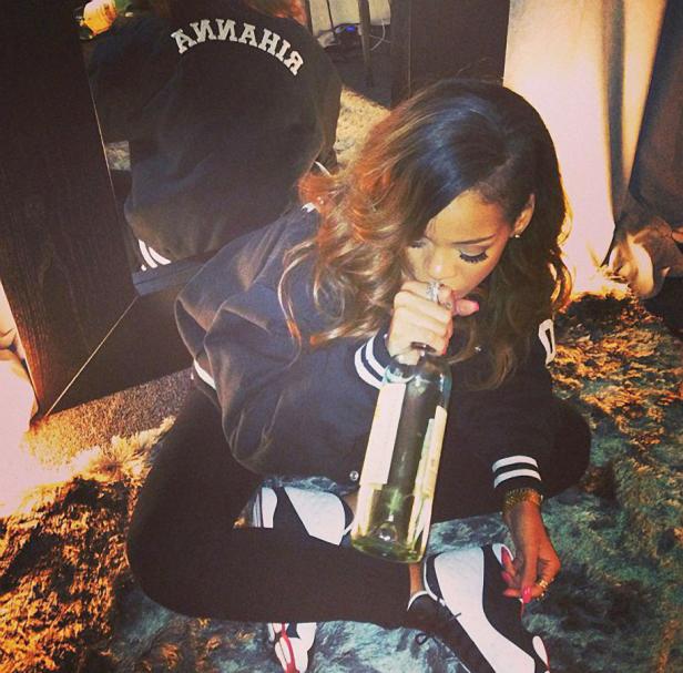 Rihanna sitzt auf einem Teppich und trinkt aus einer Weinflasche.