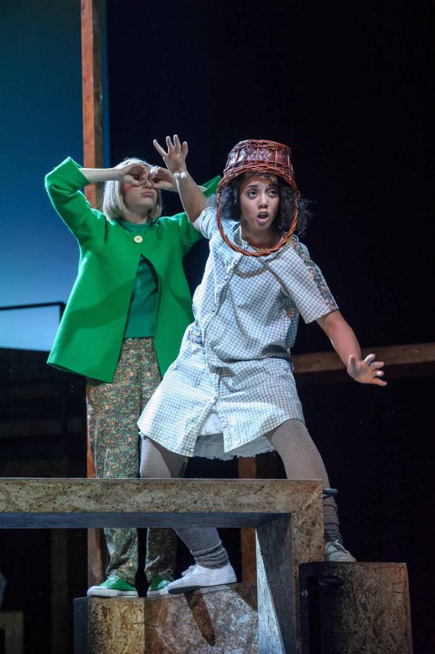 Zwei Schauspielerinnen stehen auf einer Bühne, eine mit einem Korb auf dem Kopf.