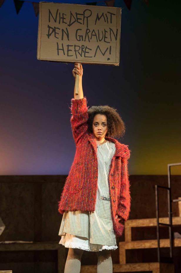 Eine junge Frau hält ein Schild mit der Aufschrift „Nieder mit den grauen Herren!“ hoch.