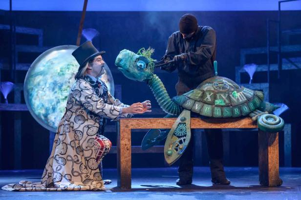 Auf einer Bühne interagieren zwei Darsteller mit einer mechanischen Schildkröte.