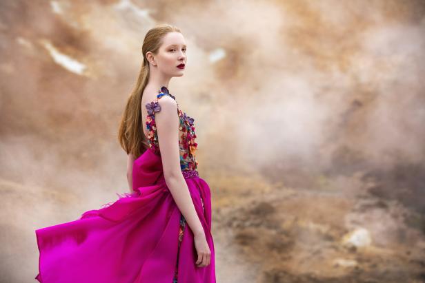 Eine Frau in einem pinkfarbenen Kleid mit Blumenapplikationen blickt über ihre Schulter.