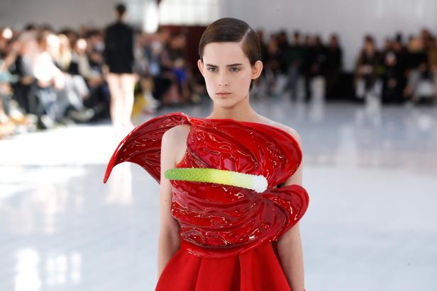 Ein Model präsentiert ein rotes Kleid mit einer großen, stilisierten Blüte auf dem Oberteil.