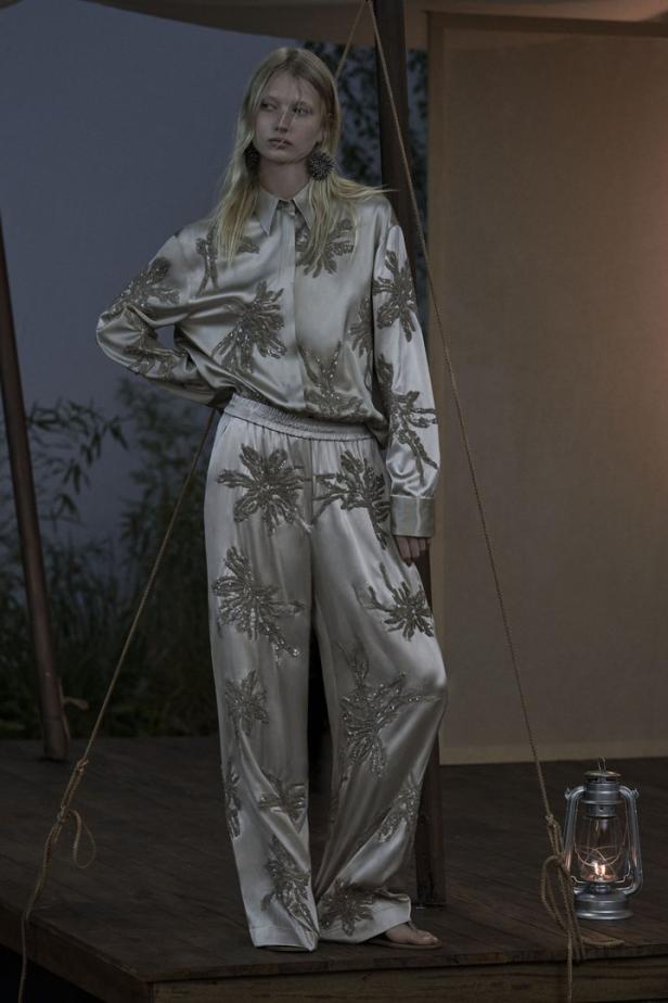 Eine Frau in einem seidenen Pyjama mit Blumenmuster steht auf einer Holzplattform.