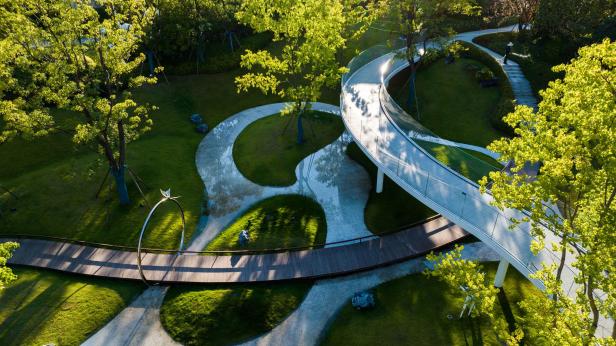 Luftaufnahme eines Parks mit geschwungenen Wegen und einer modernen Brücke.