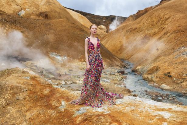 Eine Frau in einem bunten Kleid steht in einer geothermalen Landschaft Islands.