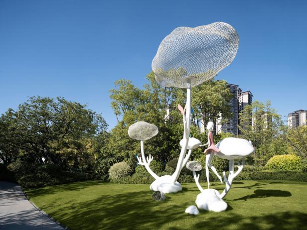 Eine skulpturale Installation mit weißen, pilzähnlichen Formen und netzartigen Wolken auf einer grünen Wiese.