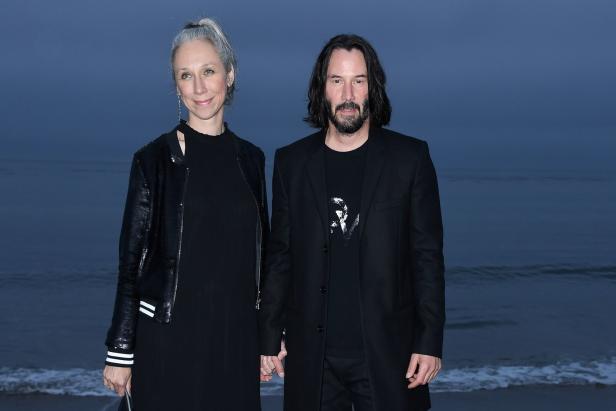 Keanu Reeves und Alexandra Grant halten Händchen vor einem dunklen Hintergrund.