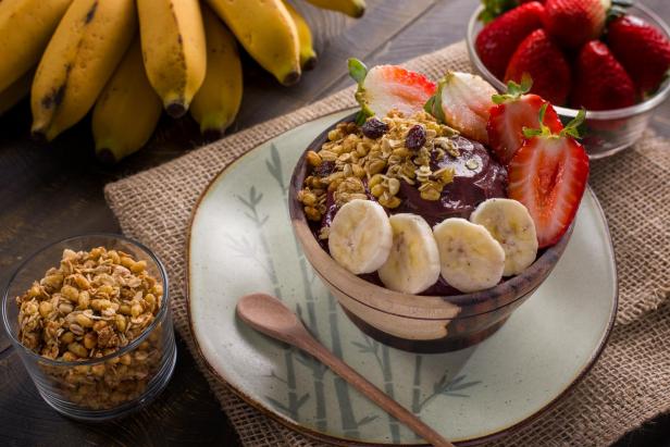 Eine Açai-Bowl mit Bananen, Erdbeeren und Müsli auf einem Tisch angerichtet.