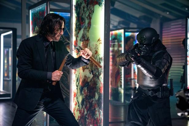 John Wick schwingt Nunchakus, während ein schwer bewaffneter Gegner auf ihn zielt.