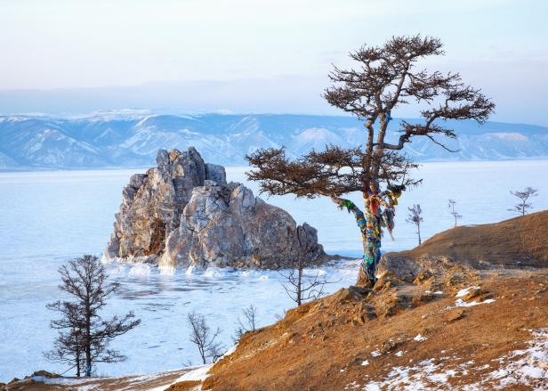 Der Schamanenfelsen ragt aus dem gefrorenen Baikalsee, mit einem Wunschbaum im Vordergrund.