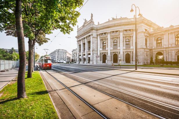 Die Wiener Ringstraße, das Burgtheater und eine Straßenbahn bei Sonnenaufgang in Wien, Österreich.