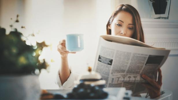 Eine Frau liest Zeitung und hält eine Tasse in der Hand.
