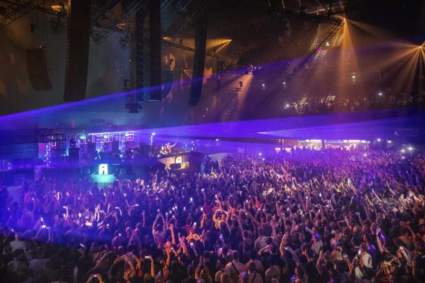Eine große Menschenmenge feiert bei einem Konzert mit blauem Laserlicht.